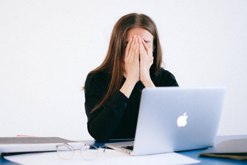 woman with hands on her face in front of a laptop - The Link Between Mental Health and Personal Finance