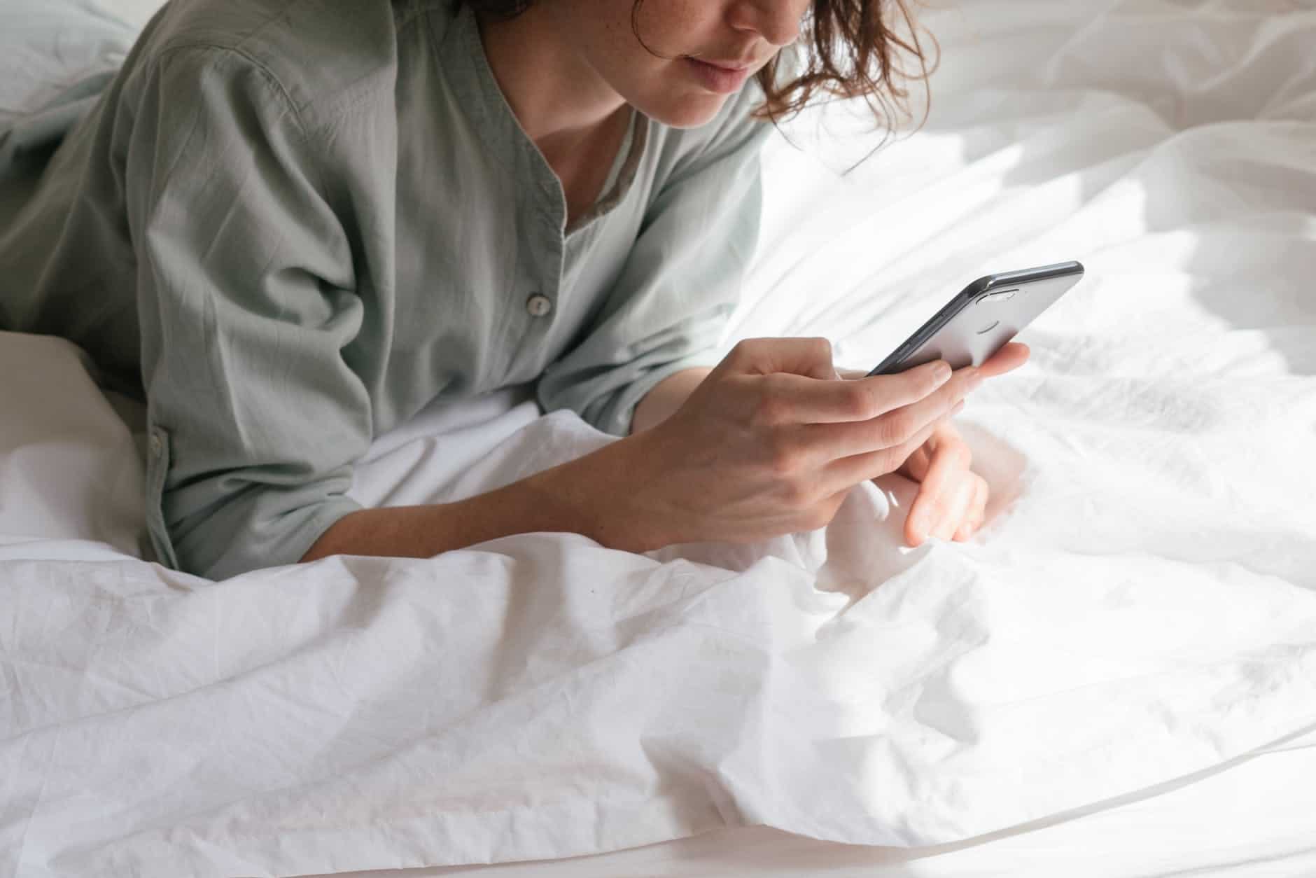 woman using a refurbished phone in bed (giffgaff phones review)