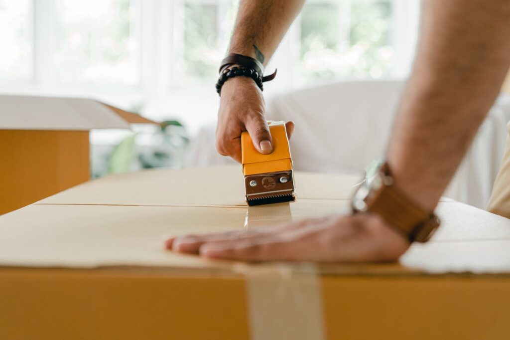 crop man packing carton box with scotch tape dispenser